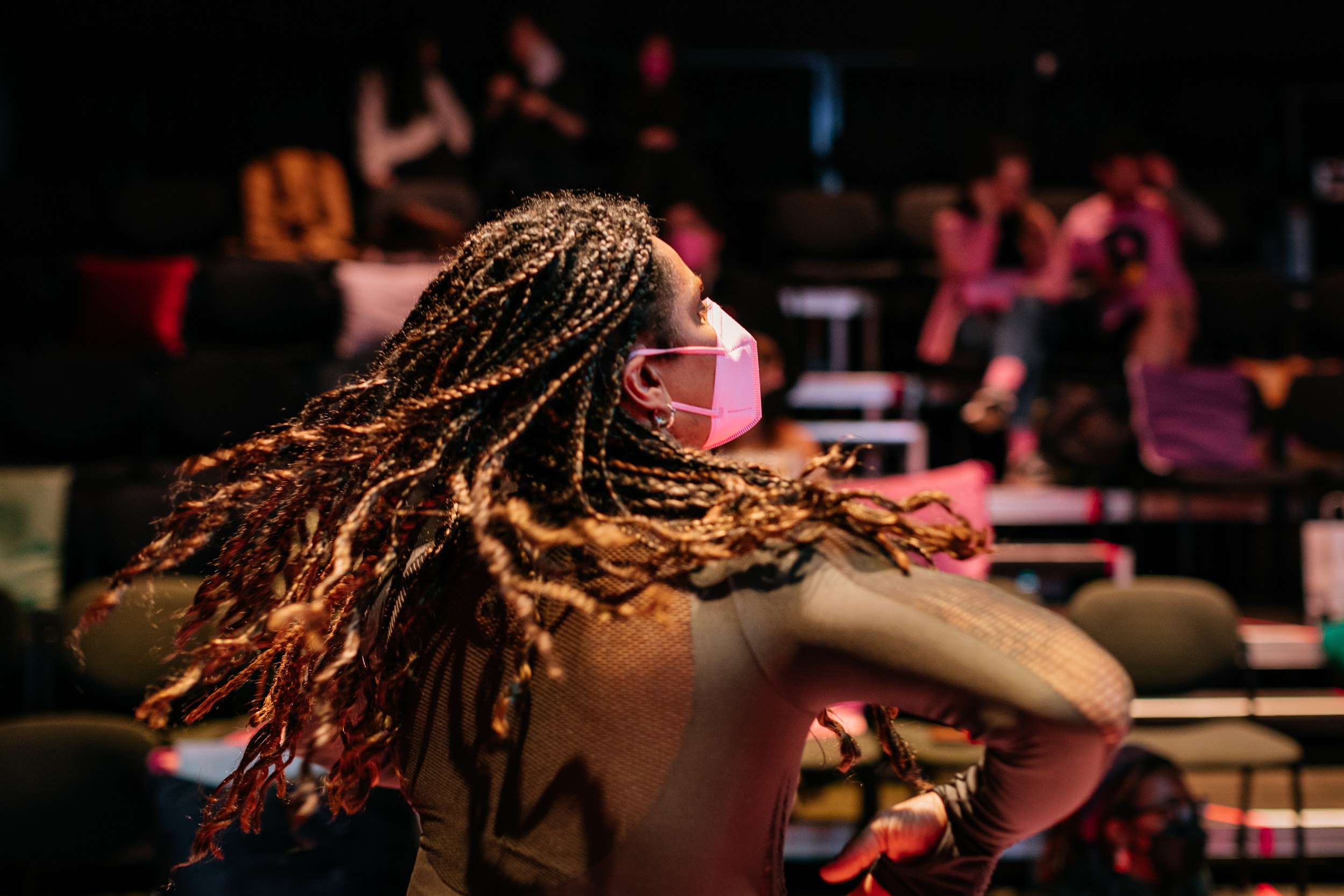 An attendee to the Disrupt afterparty is shown in the throes of dance. Their hair which they are wearing in braids which are flowing in motion. On their face is a pink facemask. Photo by Simon Lazewski.