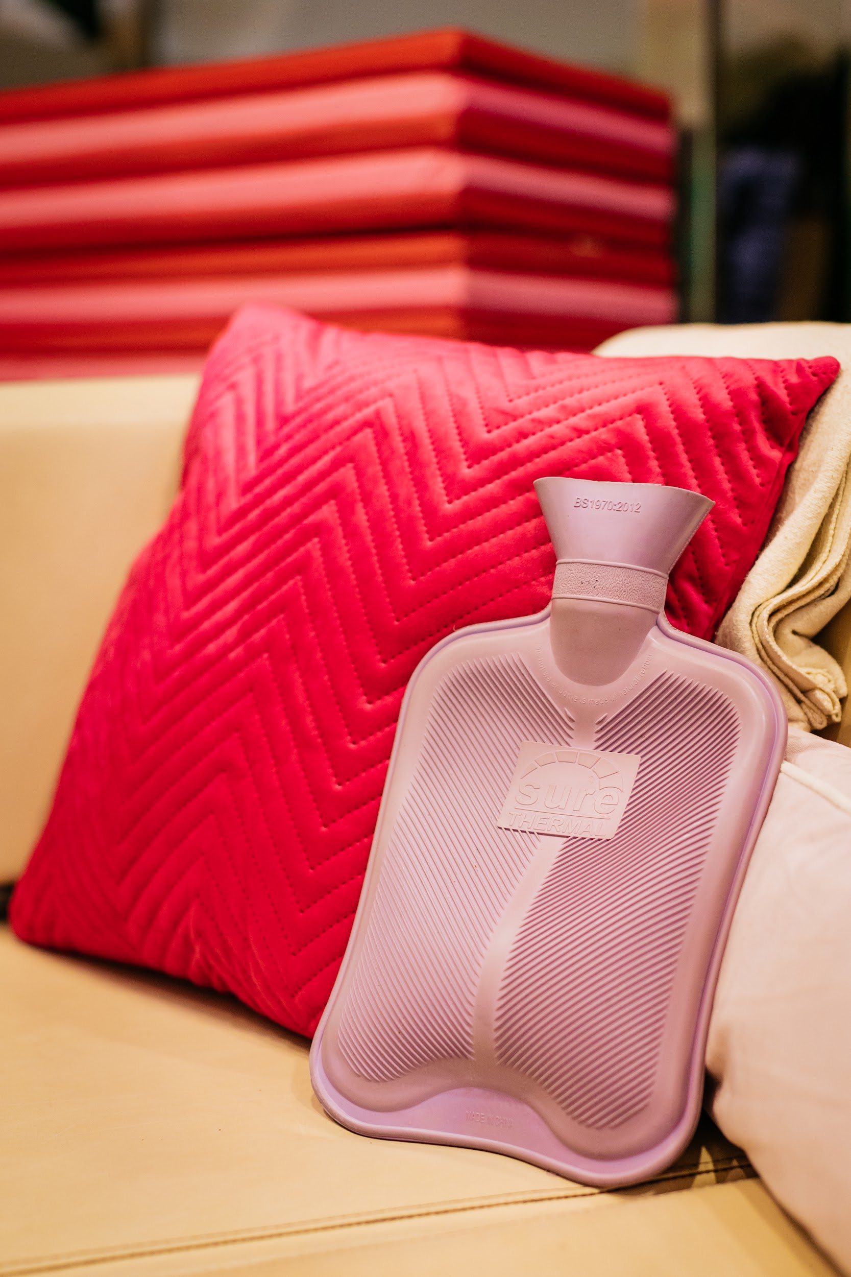 A hot water bottle rests against a cushion on a seat in Project Arts Centre. In the background are a stack of foam mats in red and pink. Photo by Simon Lazewski.